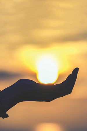 Hand holding sun during sunset